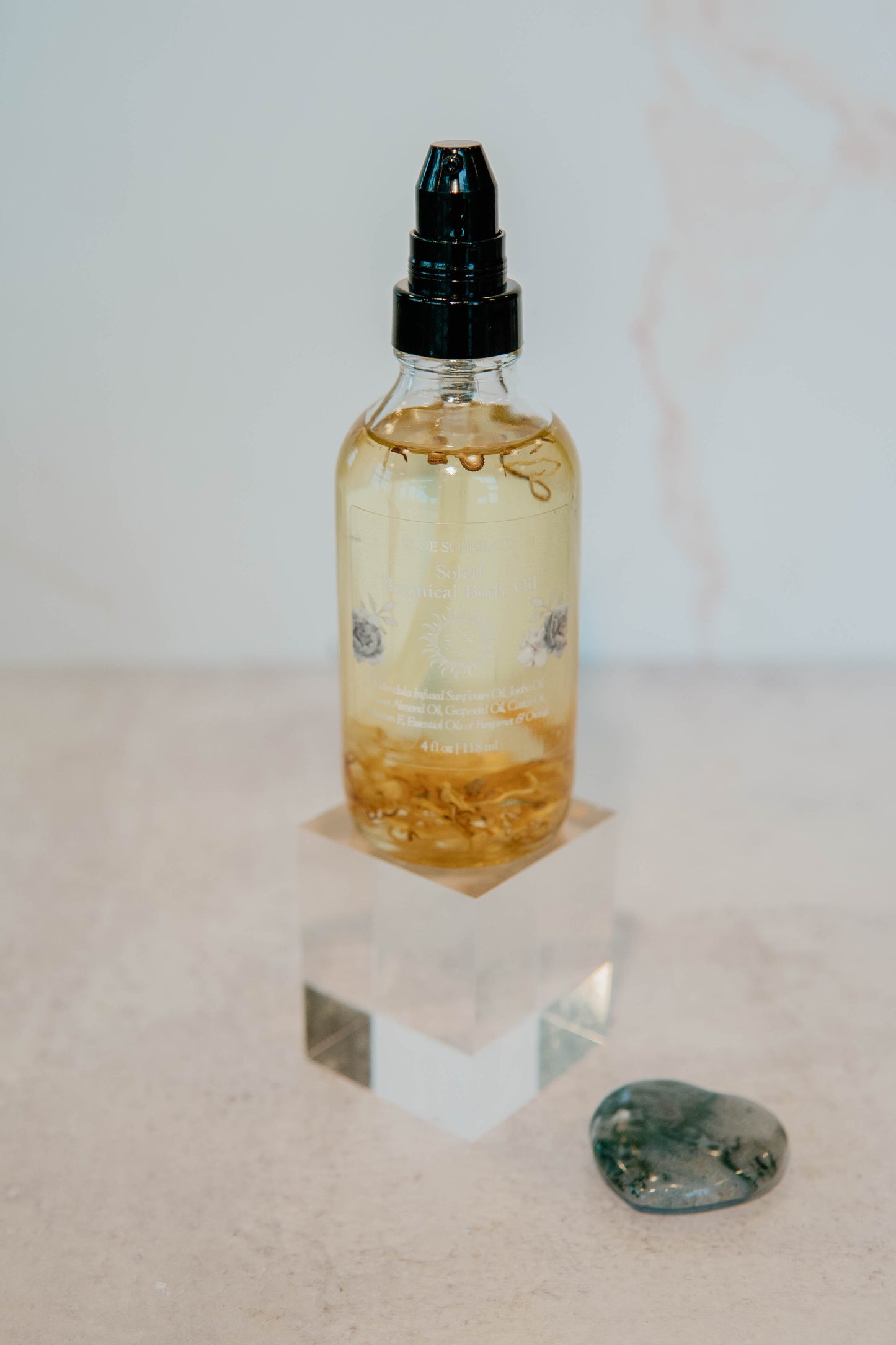 4oz clear glass bottle with black treatment pump top with botanical body oil with calendula flowers.