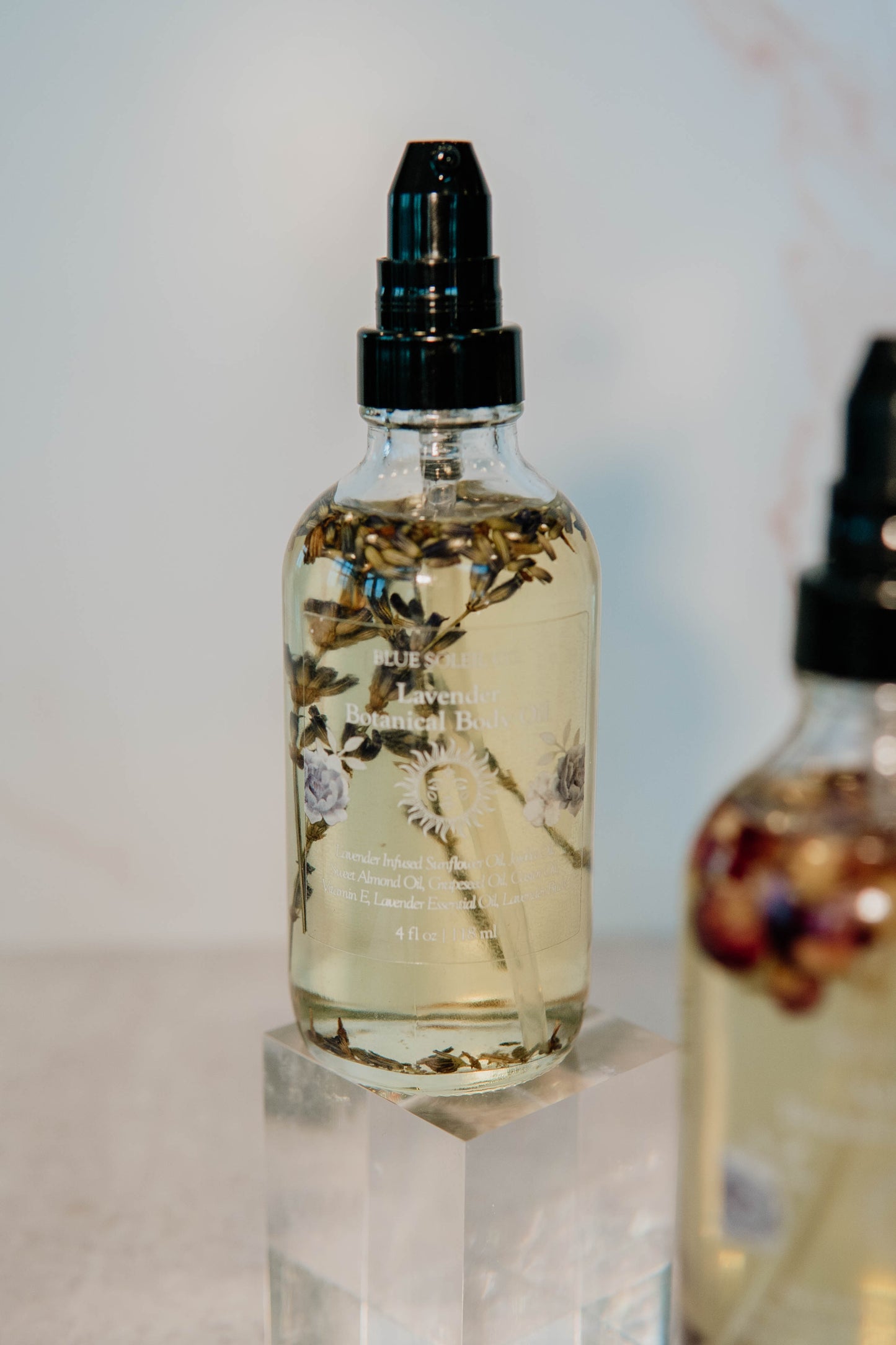  4 oz clear glass bottle with black treatment pump top with botanical body oil with lavender flowers